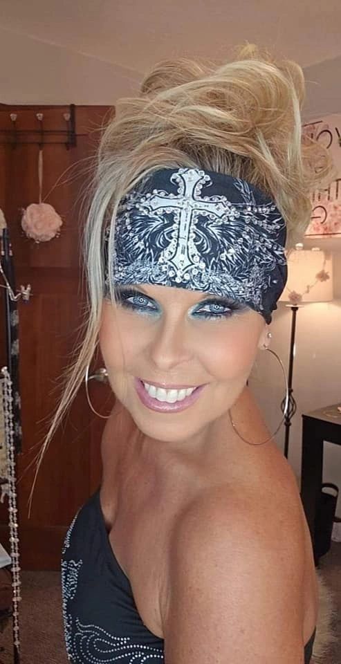 Woman with blonde hair wearing a black bandana with a white rhinestone cross design.
